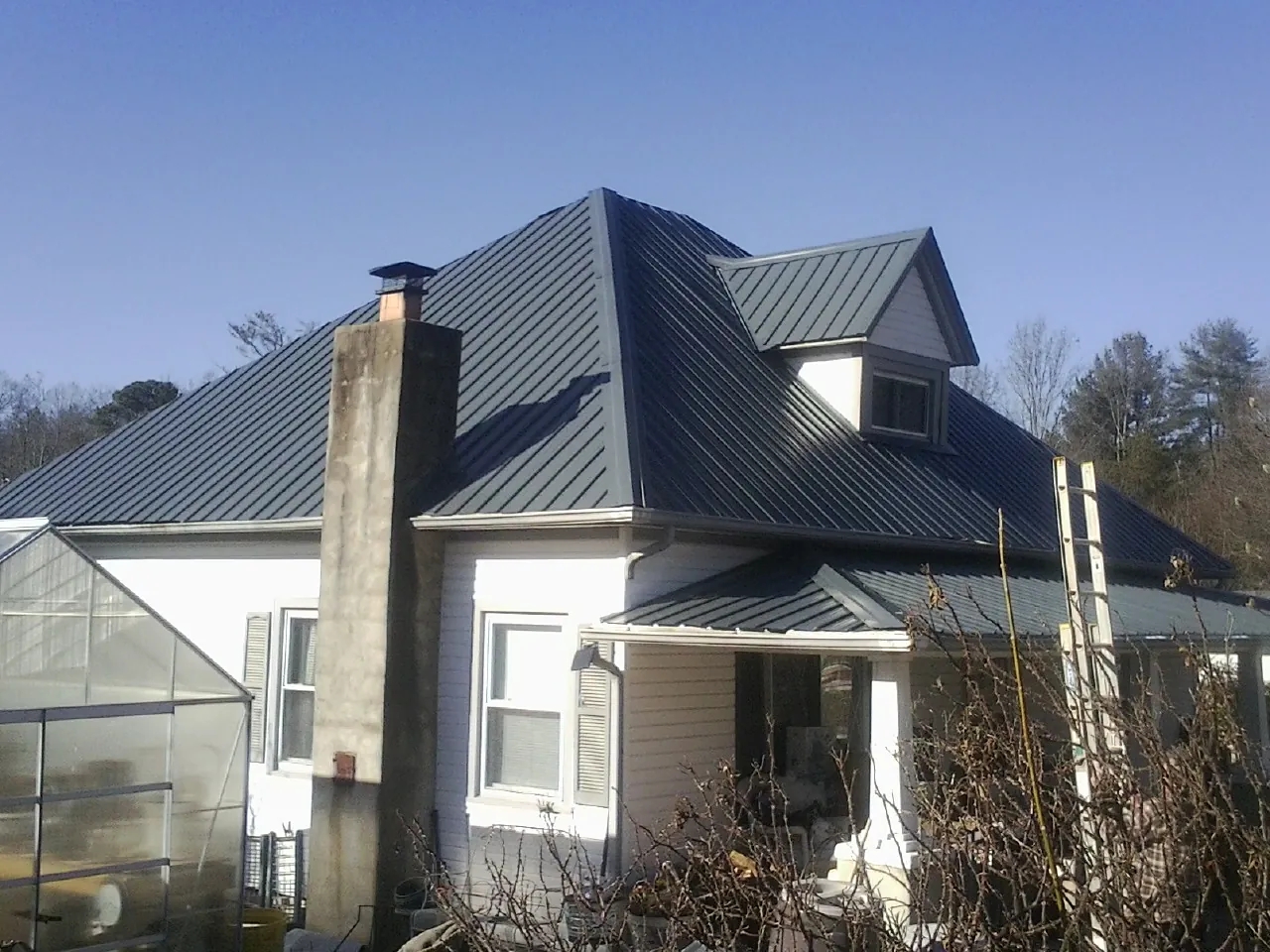 Dark blue standing seam metal roof on a white farmhouse with dormer — Slate & Tile Roof Repair by Roofing Brothers in Gates