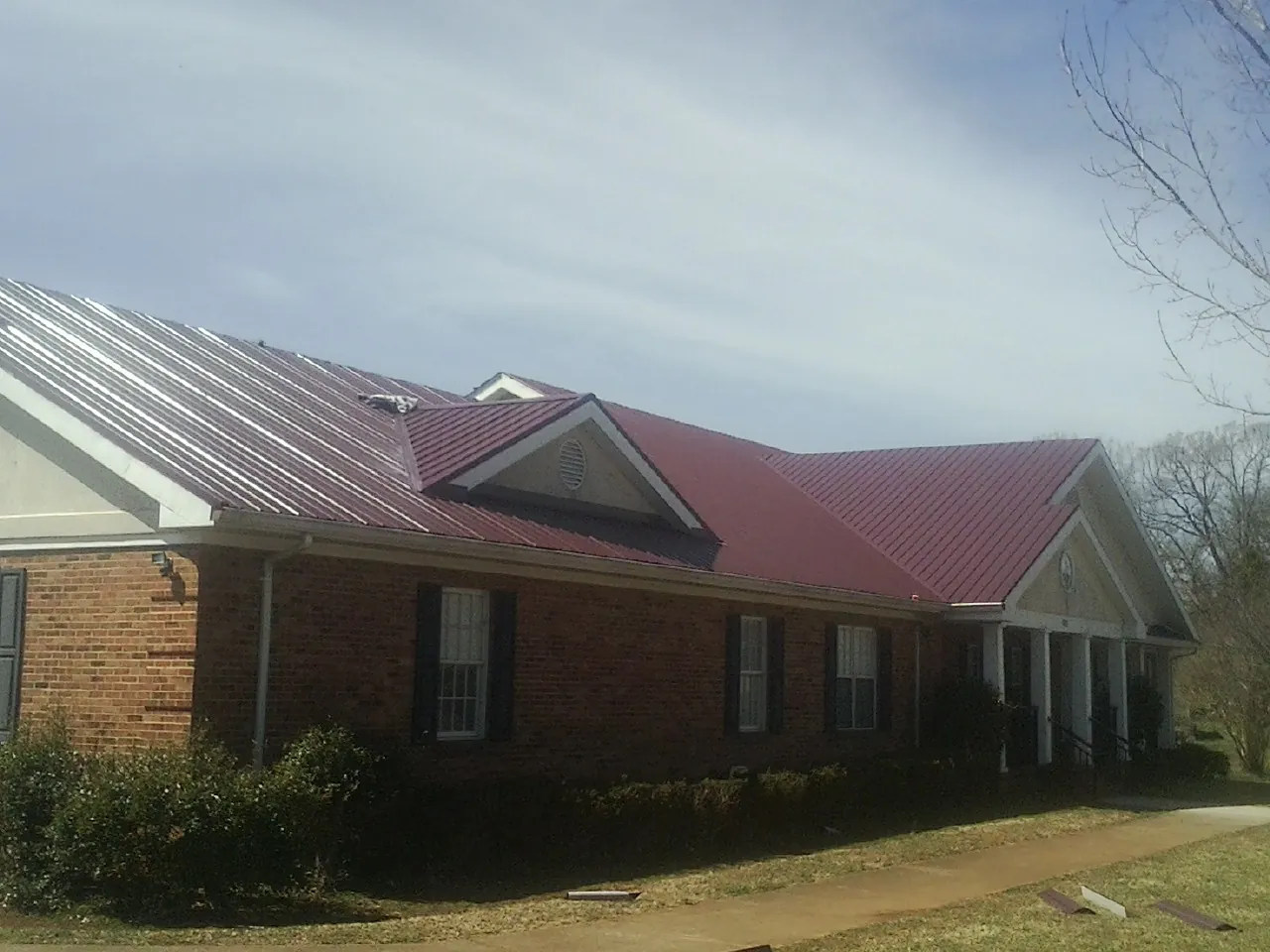 Red metal roof with gabled entries on a long brick building, from a Hail Damage Roof Repair job in Gates