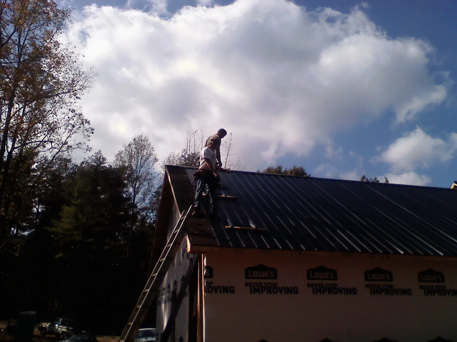 Roofer fastening dark metal panels high against a cloudy sky, from a Roof Inspection job in Gates