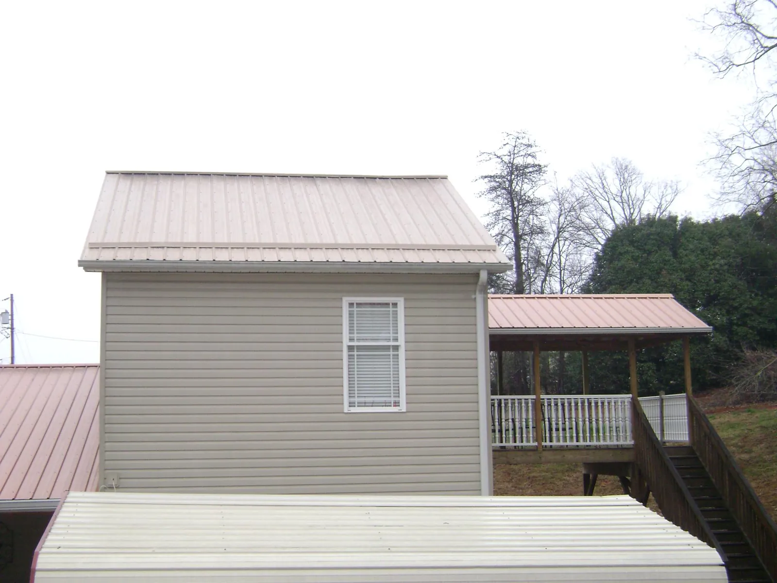 Tan metal roofs on a two story addition and attached porch, from a Roof Replacement job in Gates