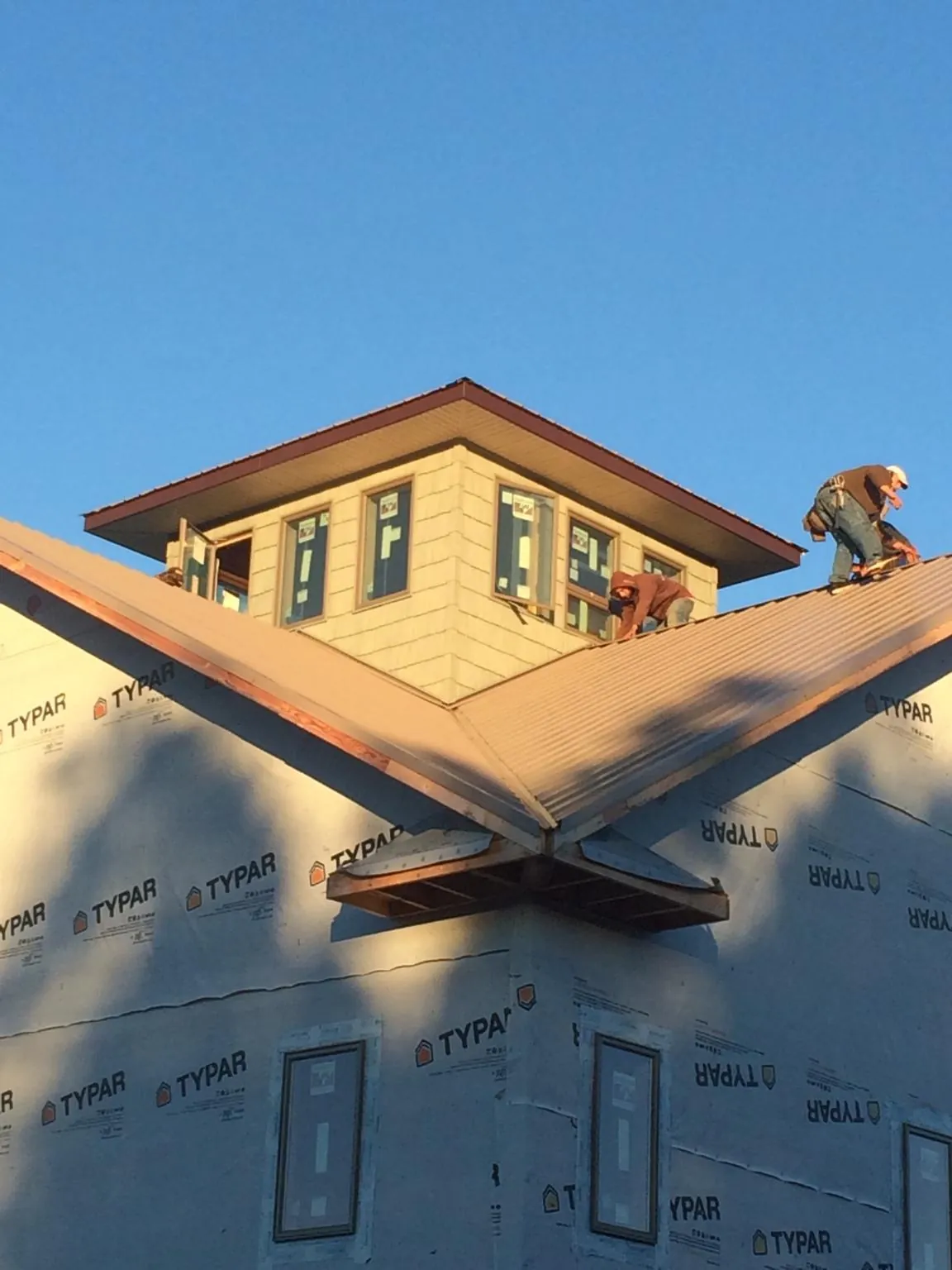 Roofers working around a rooftop cupola on a new metal roof at sunset — Roof Waterproofing in Gates by Roofing Brothers